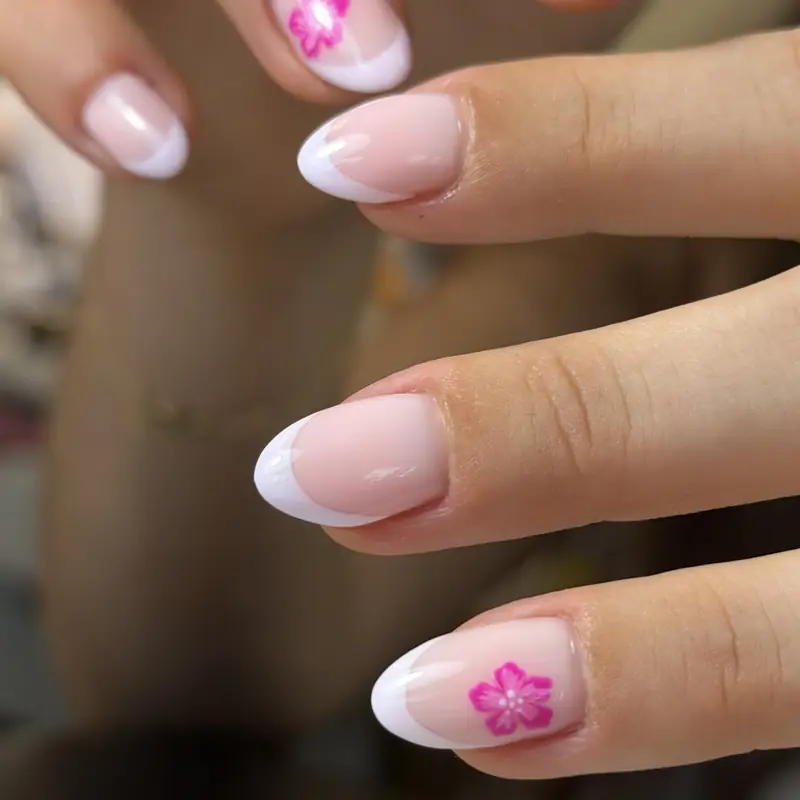 Almond nails with soft white French tips and a hand-painted pink flower accent